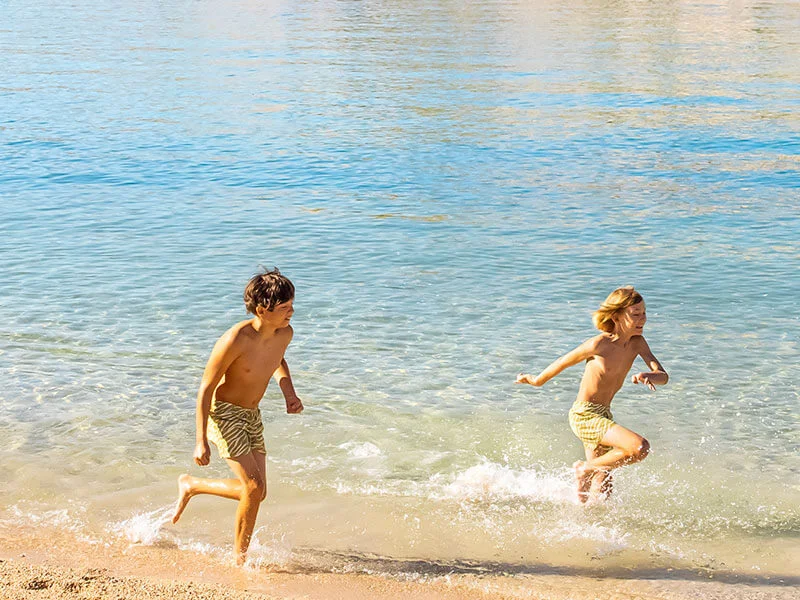 Two boys running and playing in the shallow sea at Mel Kampor beach on Rab