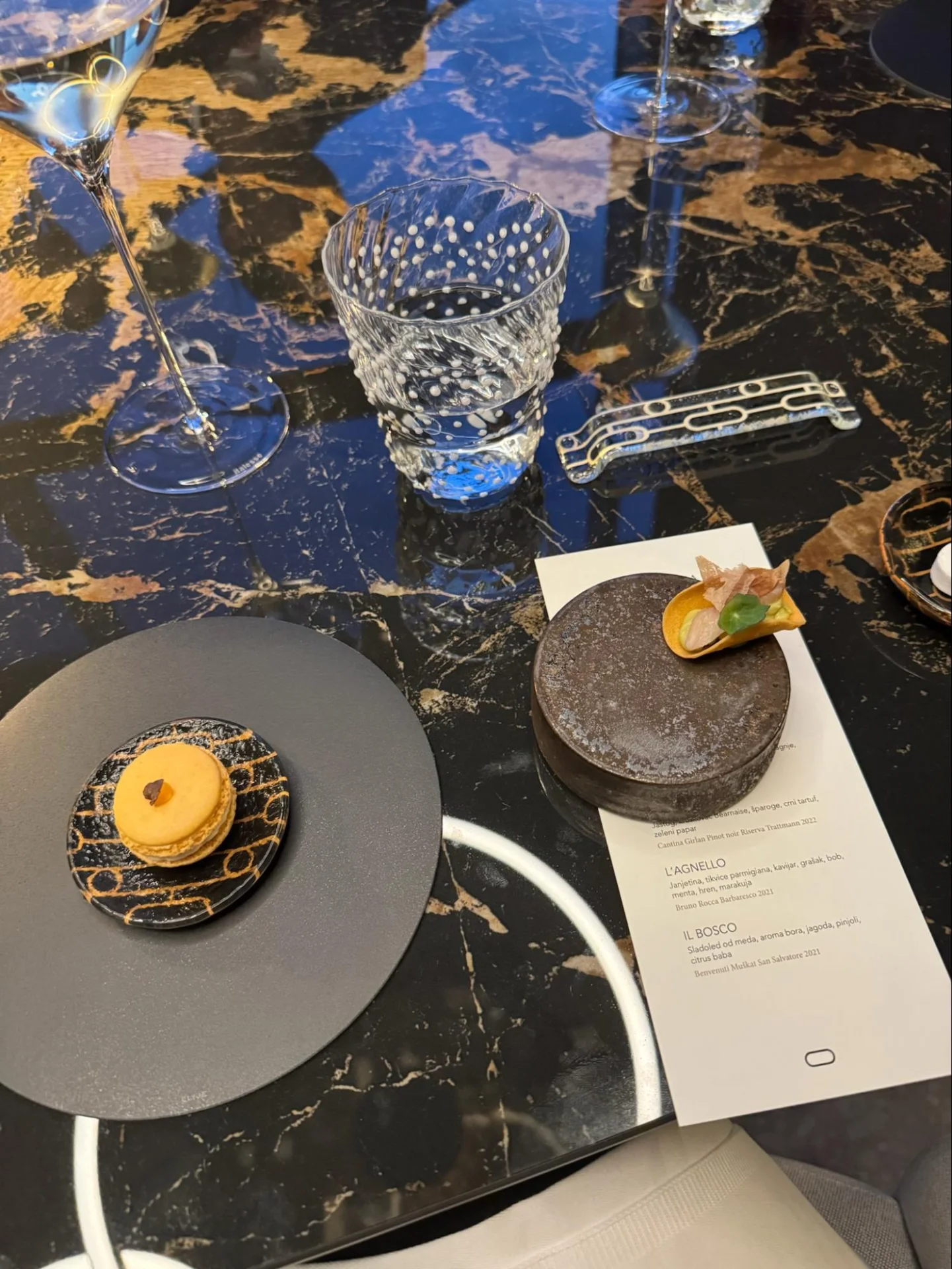 Fine dining bites, wine glasses and a tasting menu set on an elegant marble table.