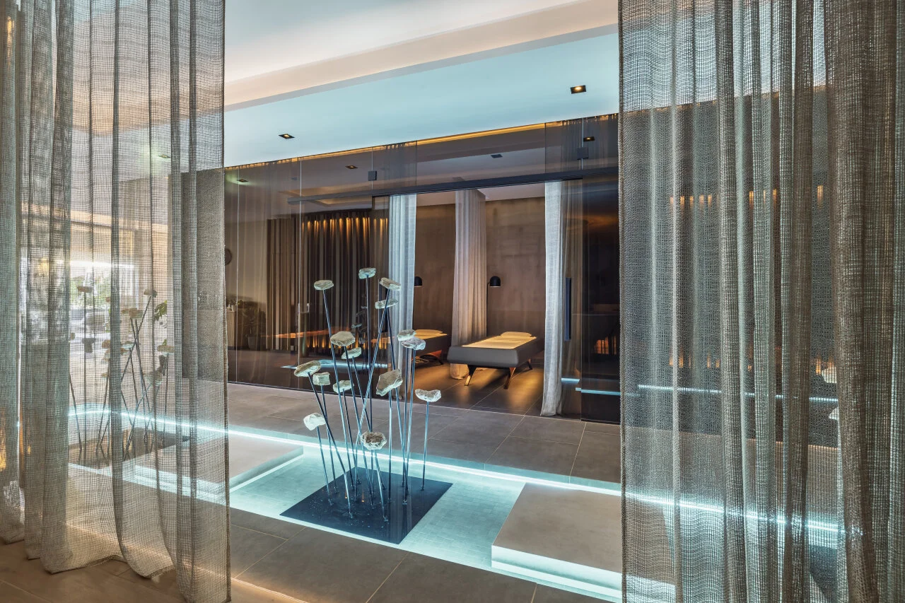 A serene spa interior with treatment beds, sheer curtains, and soft turquoise lighting.