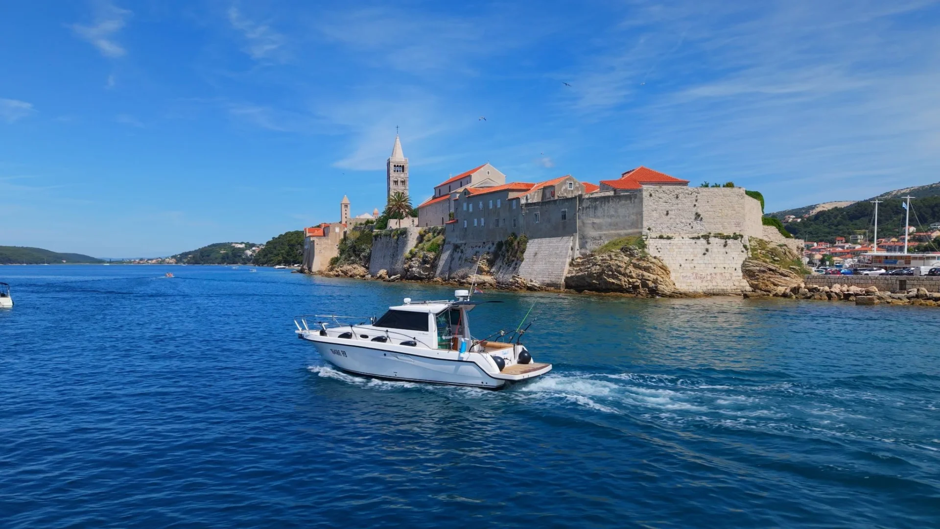 A fishing boat sails past the historic old town of Rab.