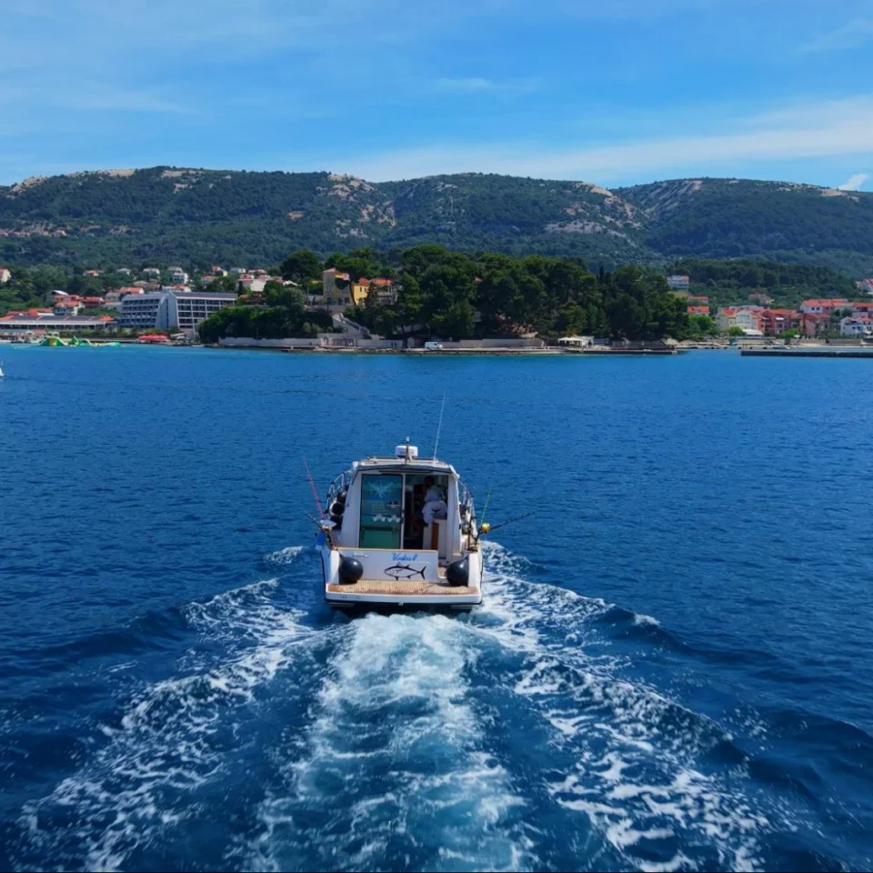 A fishing boat sails towards the coast of Rab, with views of the sea and island landscape.