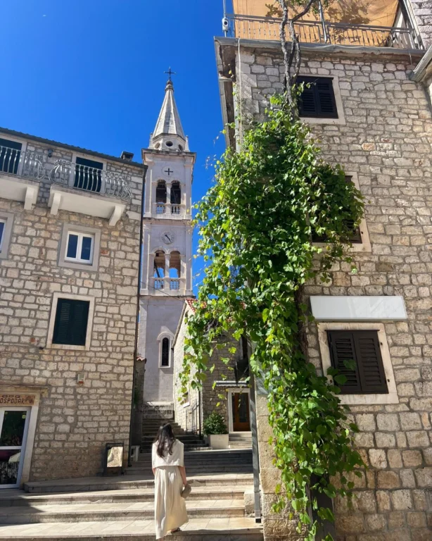 A woman walking up stone steps towards a church tower in the historic alleyways of Jelsa on Hvar.