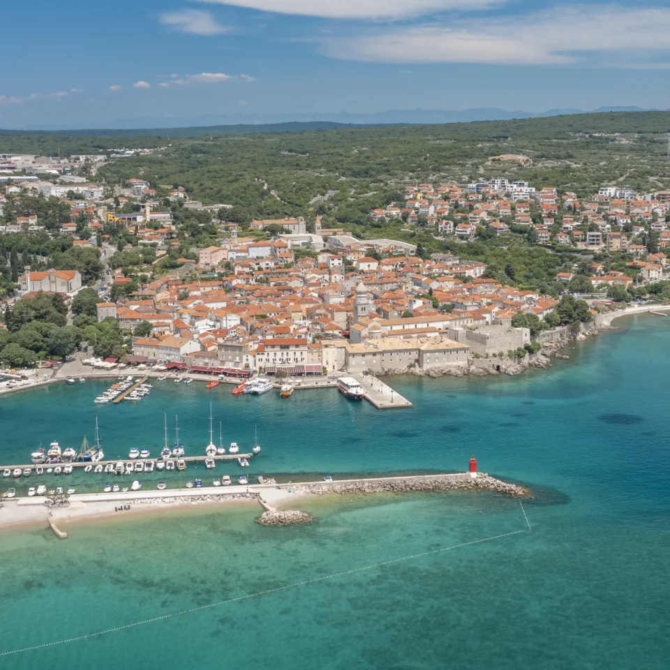 Aerial panorama of the town of Krk on the island of Krk, showing the historic centre, marina and turquoise Adriatic Sea in the background.