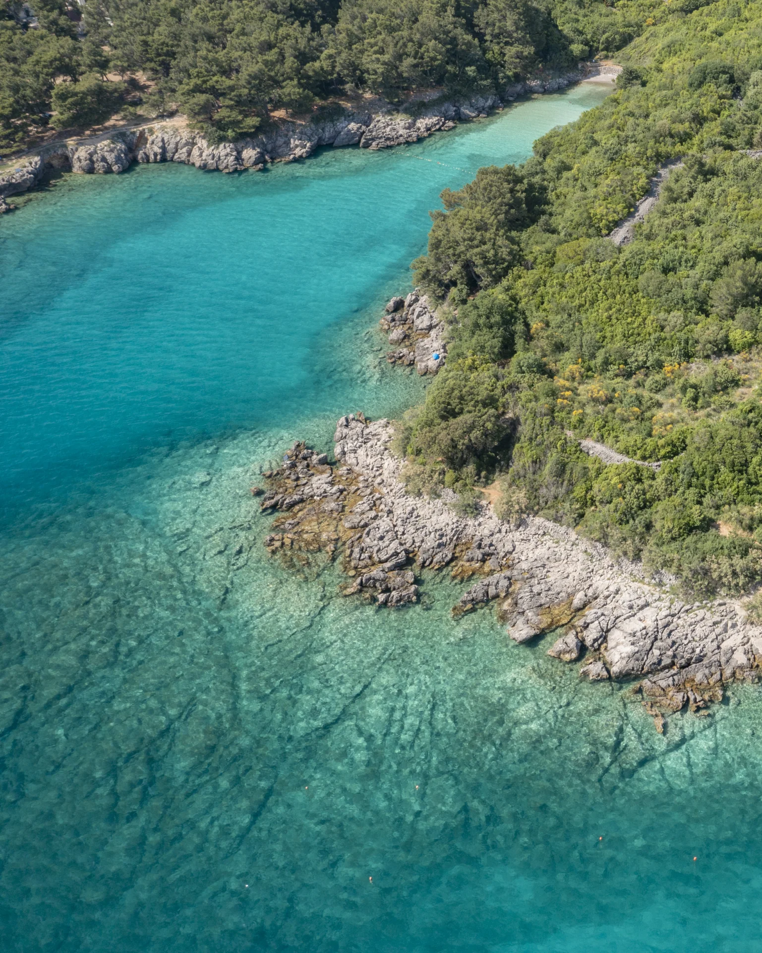 Luftaufnahme einer versteckten Bucht auf der Insel Krk mit türkisfarbenem Meer, felsiger Küste und grüner mediterraner Vegetation.
