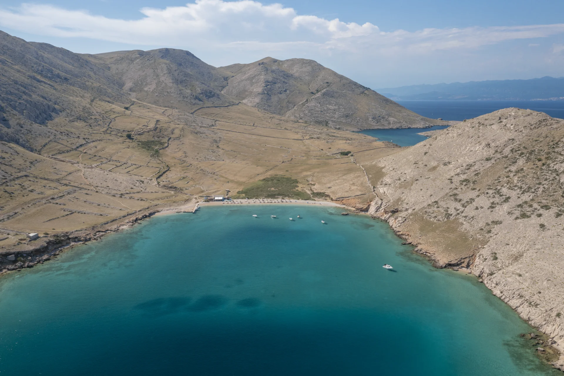 Luftaufnahme einer blauen Bucht auf der Insel Krk mit felsiger Küste und einigen Segelbooten auf dem Wasser.