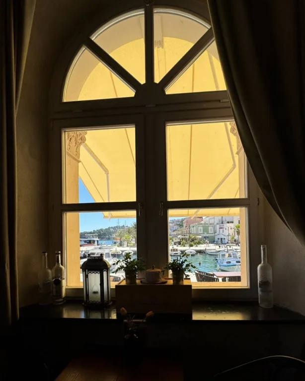 View of Jelsa harbour and boats through an arched window inside Restoran Prošperin.