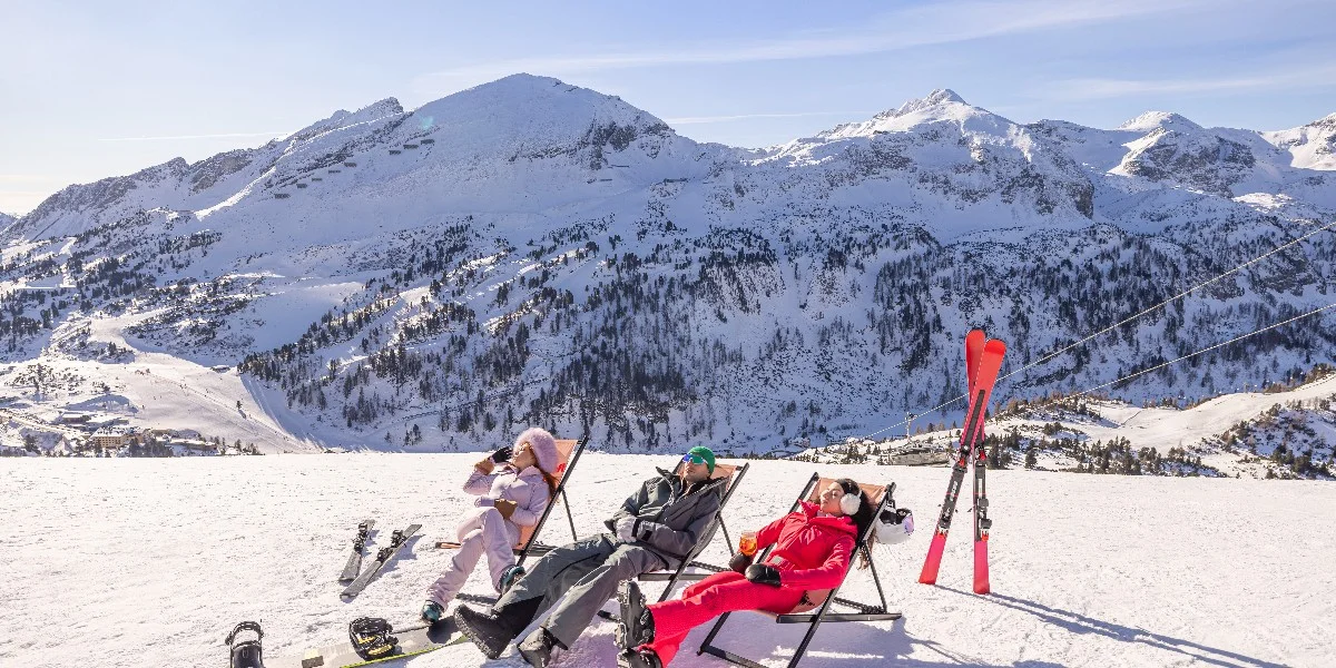 Skiers relaxing and enjoying the sunshine on the snowy slopes of Obertauern, Austria.