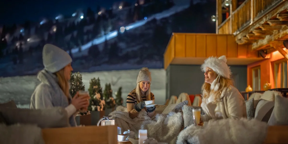 Eine Freundesgruppe genießt heiße Getränke vor dem Kesselspitze Hotel in Obertauern nach einem Tag Skifahren.
