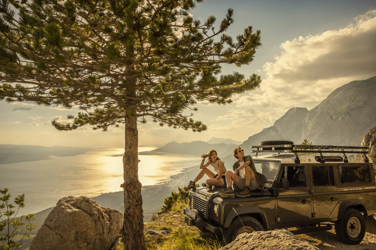 A couple sitting on a car with the sea in the back