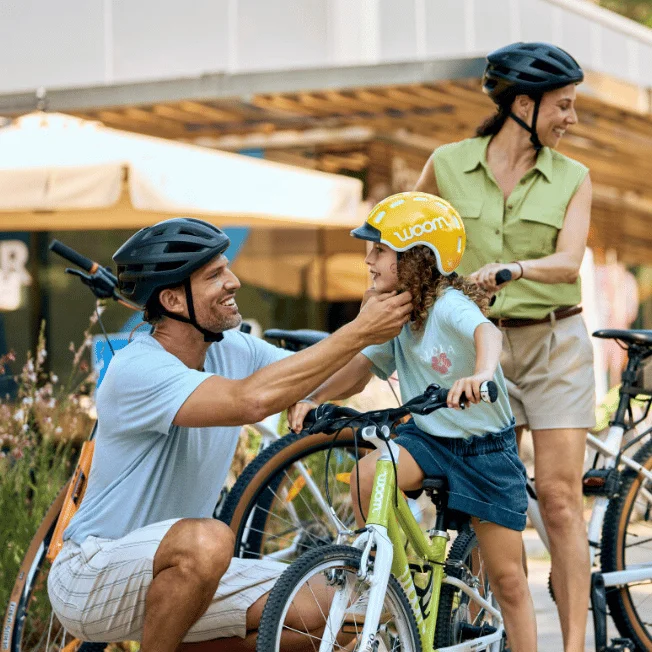 Eine Familie bereitet sich auf ein Radabenteuer vor, die Eltern helfen den Kindern mit dem Rad und Sturzhelm.