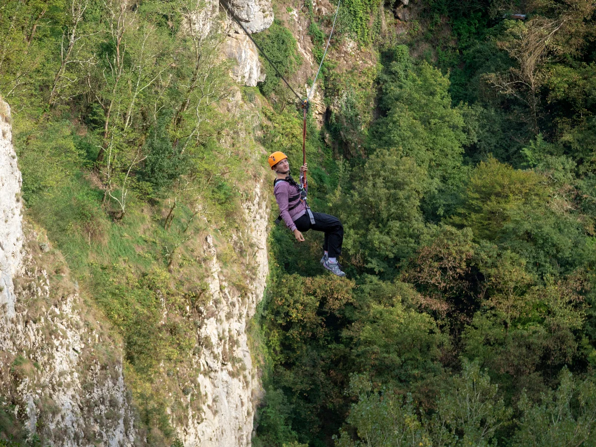 t: Osoba s kacigom i opremom spušta se zip lineom iznad Pazinske jame.
