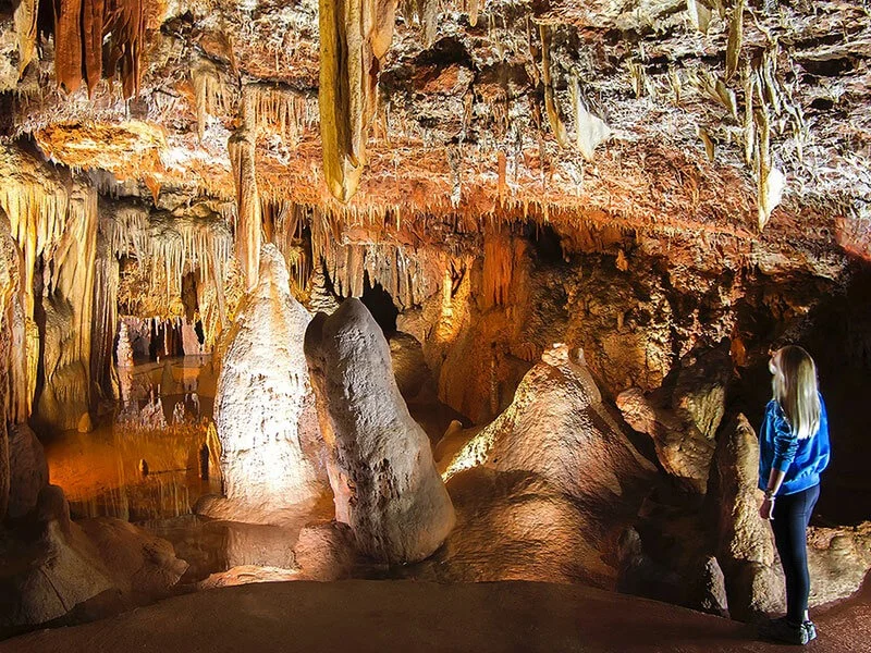 Unutrašnjost jame Baredine u Istri s bogatim stalaktitima i stalagmitima te posjetiteljicom koja razgledava osvijetljene formacije.