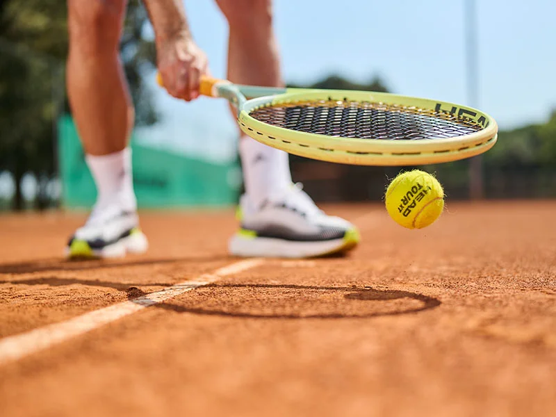 Close-up of a tennis player hitting a ball on a clay court.