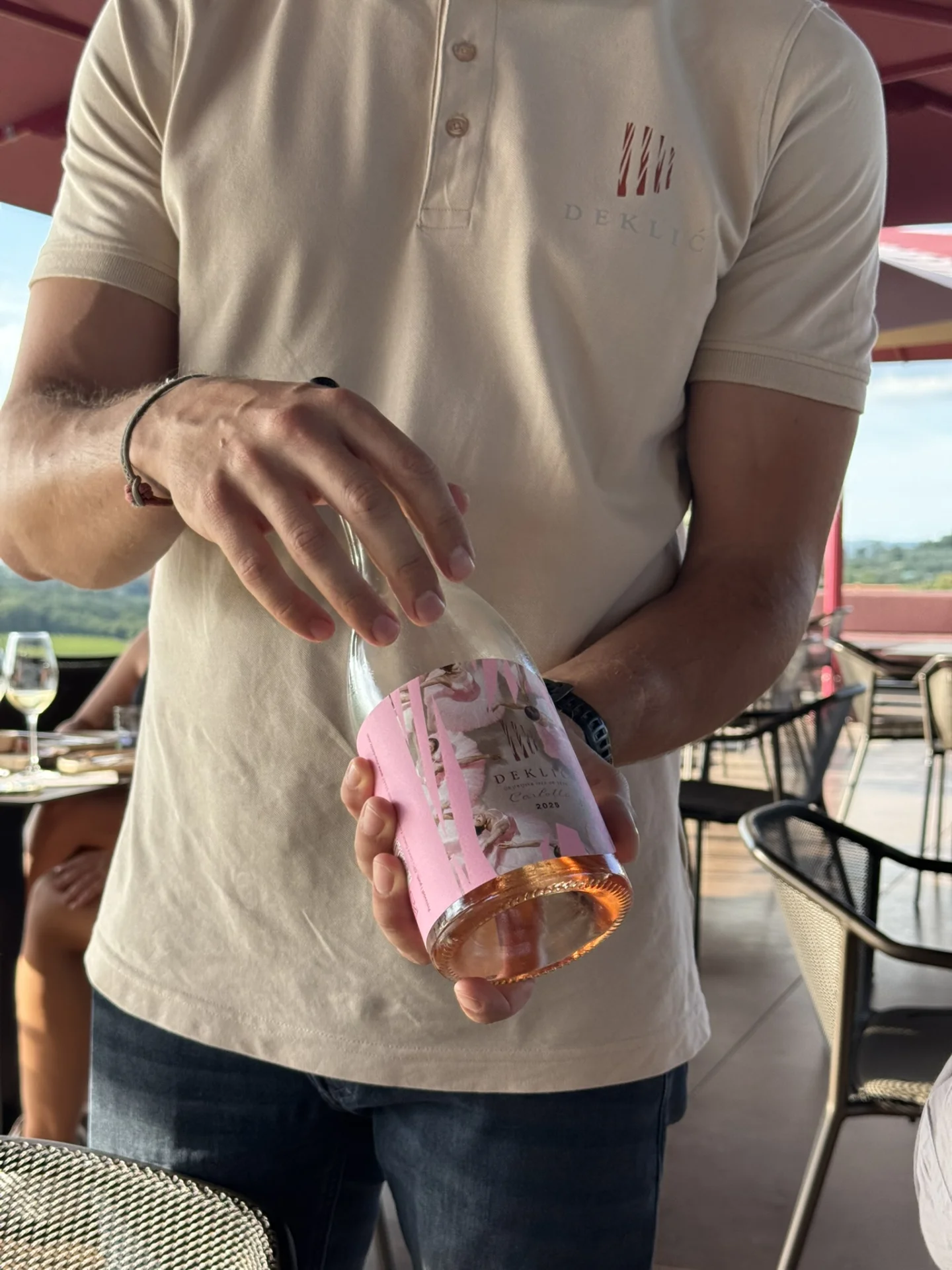 Winery staff member presenting a bottle of Deklić rosé wine during a tasting on the outdoor terrace in Istria.