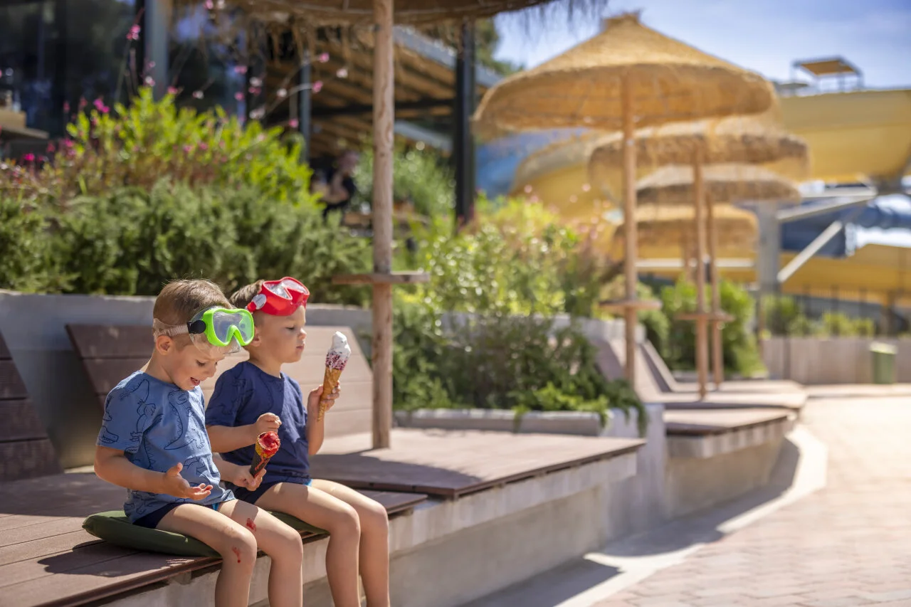 Two children relaxing by the pool and enjoying ice cream on a sunny day.